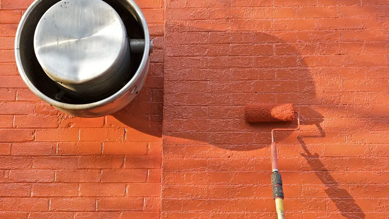 Farbroller mit roter Farbe auf einer Wand, daneben ein Farbeimer
